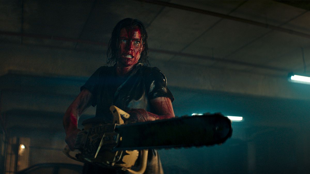 evil dead rise protagonist, a woman holding a chainsaw with blood on her face